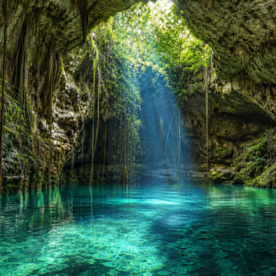 Cenote de agua turquesa entre rocas calizas y raíces en Yucatán
