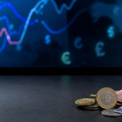 Monedas y billetes mexicanos junto a una pantalla con referencias cambiarias