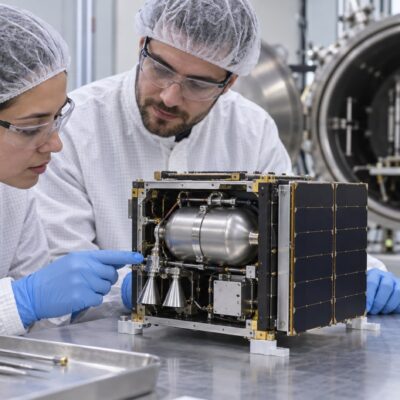 Ilustración editorial de ingenieros revisando un pequeño satélite y su sistema compacto de propulsión en un laboratorio.