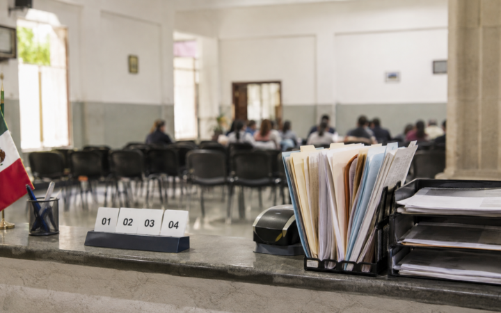 Mostrador de atención pública con documentos, turnos numerados y una sala comunitaria al fondo, imagen editorial sobre gobernabilidad.