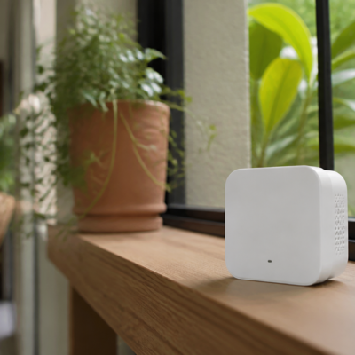 Sensor doméstico de calidad del aire sobre una mesa junto a una ventana y plantas de interior