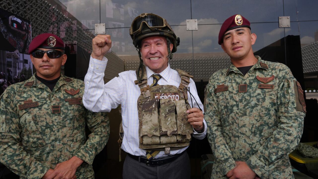 Ricardo Monreal porta chaleco y casco tácticos junto a dos militares durante una exhibición.