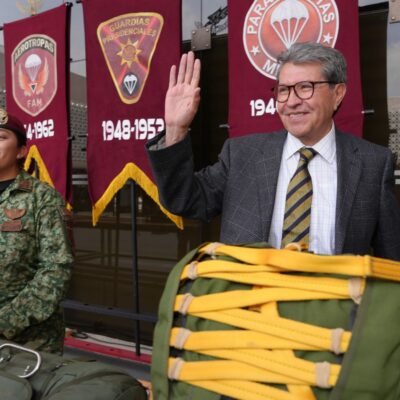 Ricardo Monreal saluda junto a una militar y equipo de paracaidismo durante una exhibición.