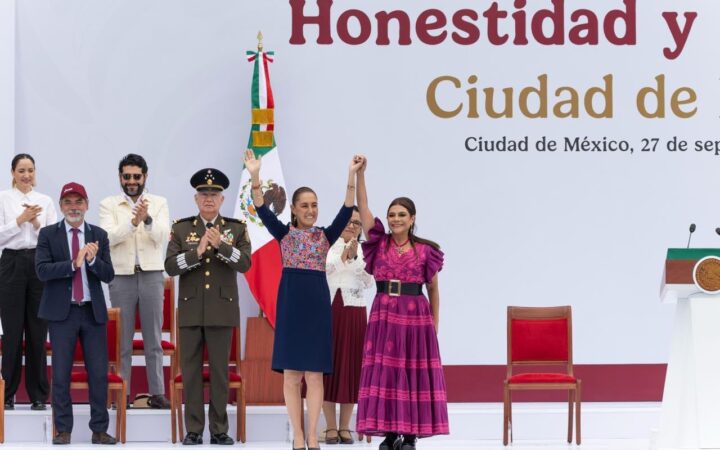 Claudia Sheinbaum y Clara Brugada levantan las manos unidas en el templete del Zócalo, acompañadas de autoridades.