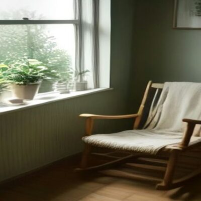Mecedora de madera con una cobija clara junto a una ventana con plantas