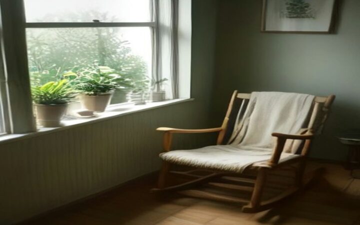 Mecedora de madera con una cobija clara junto a una ventana con plantas